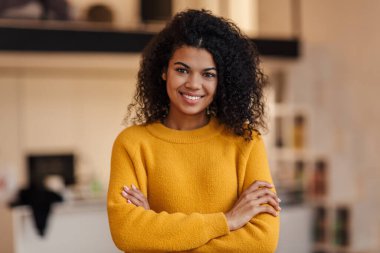 Afro-Amerikan bir kadının oturma odasında gülümseyen ve kameraya bakan görüntüsü.
