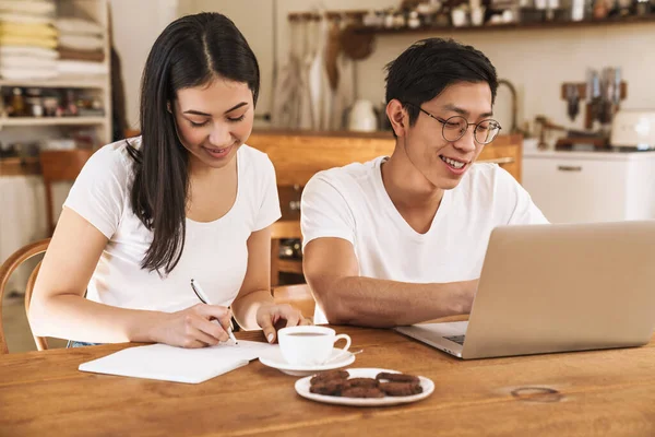 Imagen Sonriente Pareja Multicultural Tomando Notas Planificador Utilizando Ordenador Portátil —  Fotos de Stock