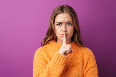 Mor arka planda izole bir şekilde duran, süveter giyen sevimli, ciddi bir genç kızın portresi, sessizlik jesti gösteriyor.