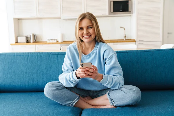 Imagen Una Joven Mujer Alegre Usando Teléfono Inteligente Sonriendo Mientras —  Fotos de Stock