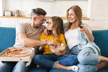 Güzel beyaz bir ailenin evde televizyon izlerken patlamış mısır ve pizza yediği fotoğraf.