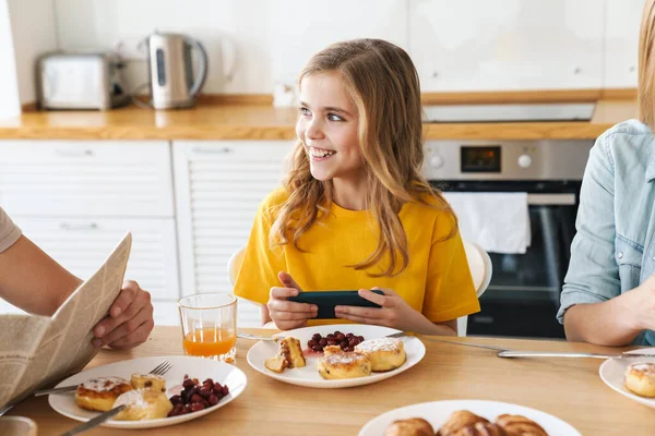 Modern mutfakta ailesiyle kahvaltı ederken video oyunu oynayan komik bir kızın fotoğrafı.