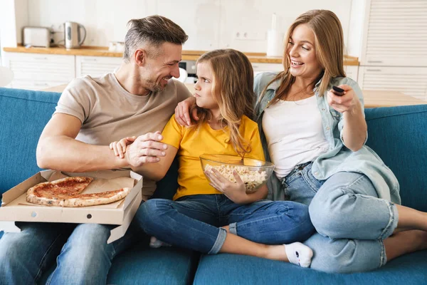 Güzel beyaz bir ailenin evde televizyon izlerken patlamış mısır ve pizza yediği fotoğraf.
