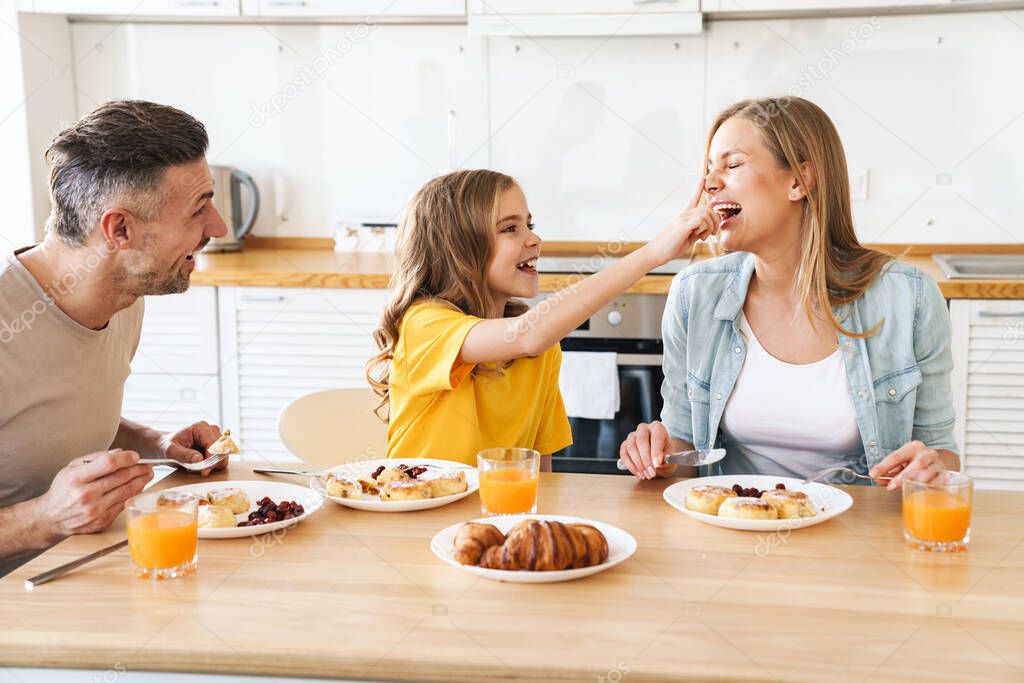 Photo of funny caucasian beautiful family laughing while having breakfast in modern kitchen