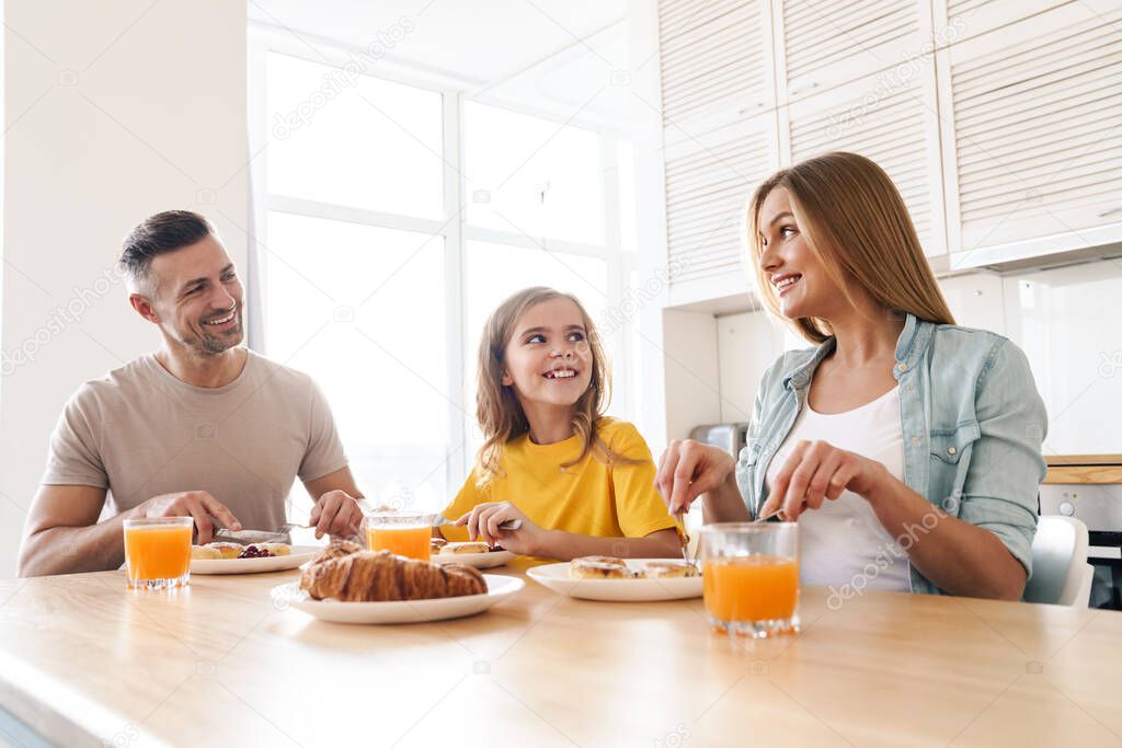Photo of happy caucasian beautiful family smiling and talking while having breakfast in modern kitchen