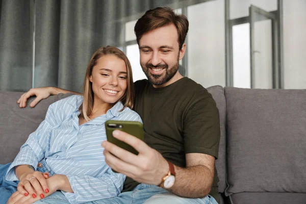 Photo Cheerful Beautiful Couple Smiling Using Mobile Phone While Sitting — Stock Photo, Image