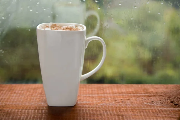 Filiżanka kawy z pianką na tle okna deszczowy dzień — Zdjęcie stockowe