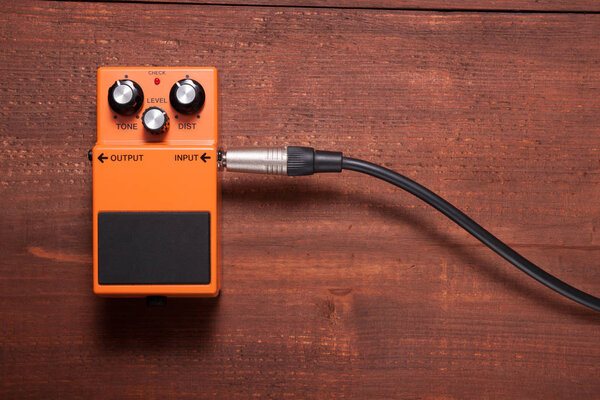 Orange guitar pedal with cable on the wooden background