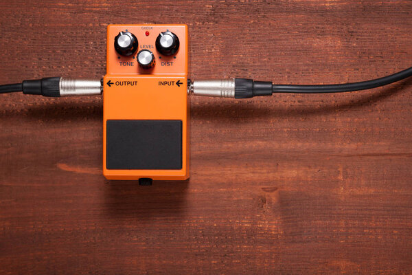 Orange guitar pedal with cable on the wooden background