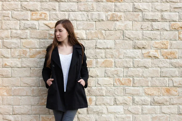Dziewczyna w czarnym płaszczu w pobliżu mur z cegły — Zdjęcie stockowe