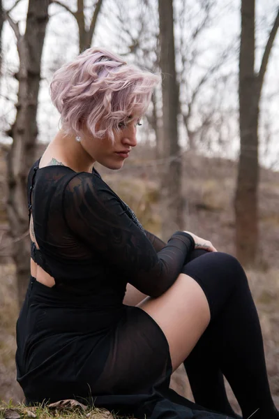 Retrato de uma jovem sentada na floresta em vestido preto e — Fotografia de Stock