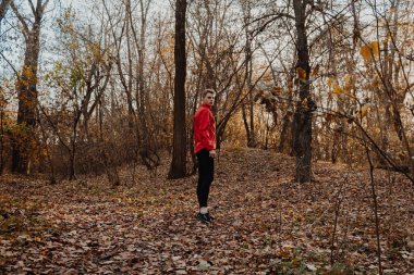 Kırmızı rüzgarlıklı bir adam sonbahar ormanında koşar..