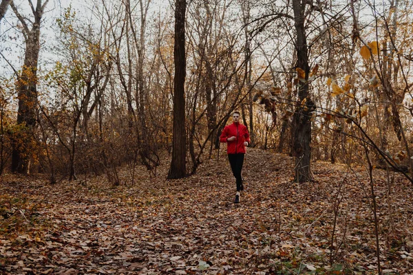 Egy piros széldzsekis fickó fut az őszi erdőben.. — Stock Fotó