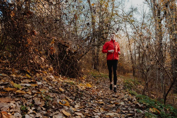 Egy piros széldzsekis fickó fut az őszi erdőben.. — Stock Fotó