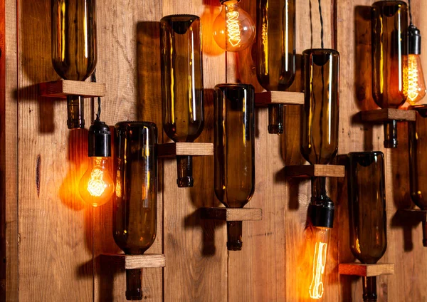 空のワインボトルと白熱灯と木製の壁. — ストック写真
