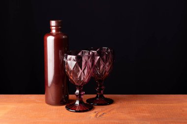 Seramik şarap şişesi ve tahtanın üzerinde iki kırmızı yüzlü bardak.