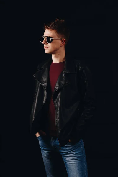 一个戴着太阳镜 穿着黑色背景皮夹克的年轻人的画像 — 图库照片