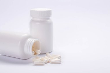 Beyaz arka planda iki kavanoz ilaç ve dağınık haplar.