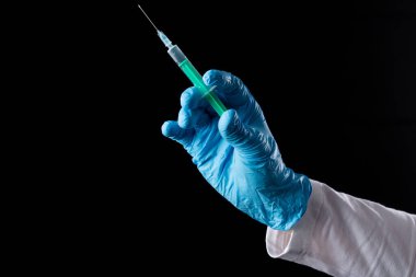 Mavi eldivenli bir el siyah arka planda bir şırınga tutar.