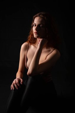 Karanlık bir stüdyoda genç bir kıvırcık kızın portresi.