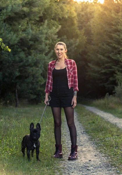 Hipster chica con tatuaje caminando francés Bulldog en el bosque — Foto de Stock