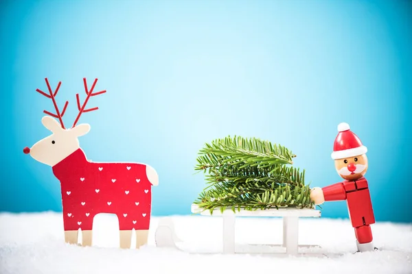 Vicces télapó és a rénszarvas hordoz karácsonyfa a hóban — Stock Fotó