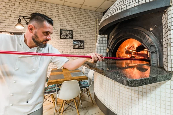 Handsome man baking pizza in woodfired oven