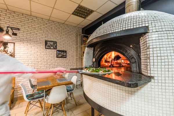 Handsome man baking pizza in woodfired oven