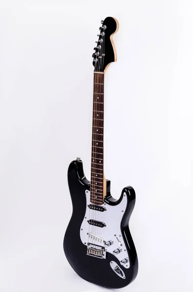 The classical form of black and white electric guitar standing upright with wooden maple neck
