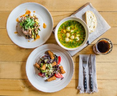 Akşam yemeği: çorba köfte ve otlar, peynir, domates ve otlar, salata ile et ve otlar, ekmek, bir bardak içki ve çatal bıçak takımı, ahşap bir masa üzerinde ile bisküvi ile. Yukarıdan görüntülemek