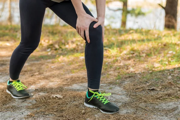 Chica en pantalones deportivos y zapatos, de pie aferrándose a la rodilla , — Foto de Stock