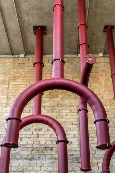 Красные металлические трубы, свисающие с потолка на фоне кирпичной стены — стоковое фото