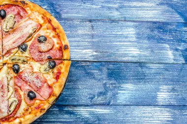 Et, zeytin, peynir ve mantar, mavi kot arka plan üzerinde yarım yuvarlak pizza