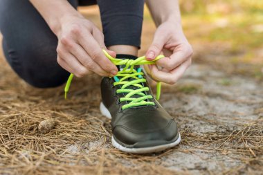 Bağlama ayakkabı bağcığı spor üzerinde oturan kız spor pantolon ve kapüşonlu,