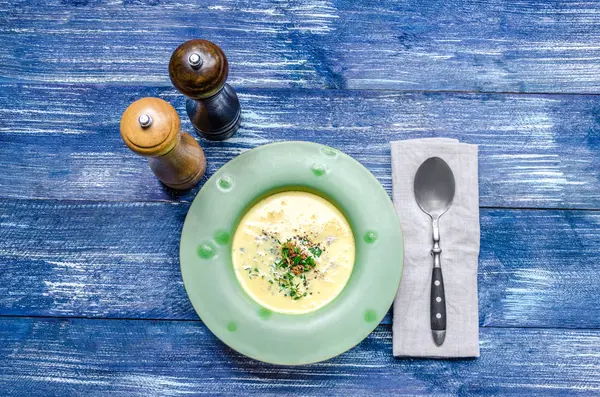 Et ve otlar, bir kaşık ve baharat mavi kot arka plan üzerinde yeşil bir plaka ile sarı peynir çorbası — Stok fotoğraf