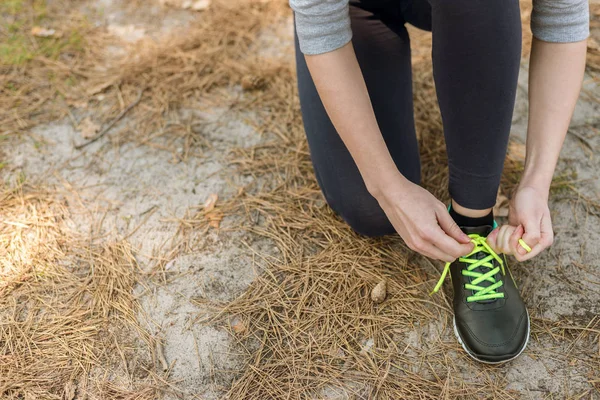 Girl in sports pants and hoodie, sitting tying shoelaces on spor