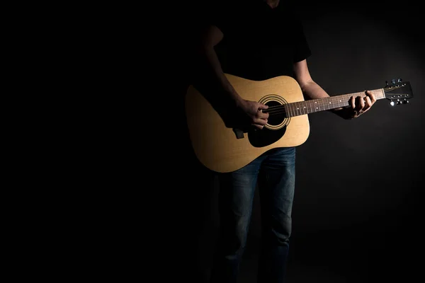 Il chitarrista in jeans suona una chitarra acustica, sul lato destro del telaio, su uno sfondo nero. Telaio orizzontale — Foto Stock