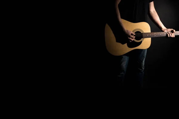 Il chitarrista in jeans suona una chitarra acustica, sul lato destro del telaio, su uno sfondo nero. Telaio orizzontale — Foto Stock