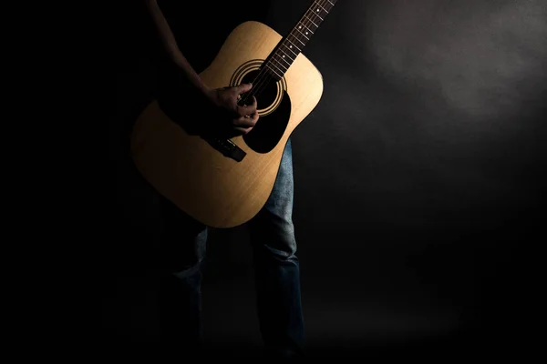Der Gitarrist in Jeans spielt eine Akustikgitarre, auf der linken Seite des Rahmens, auf schwarzem Hintergrund. horizontaler Rahmen — Stockfoto