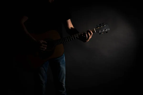 Il chitarrista in jeans suona una chitarra acustica, sul lato sinistro del telaio, su uno sfondo nero. Telaio orizzontale — Foto Stock