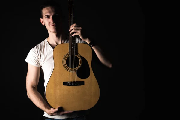 Guitarist, music. A young man stands with an acoustic guitar on a black isolated background. Horizontal frame — Stock Photo, Image