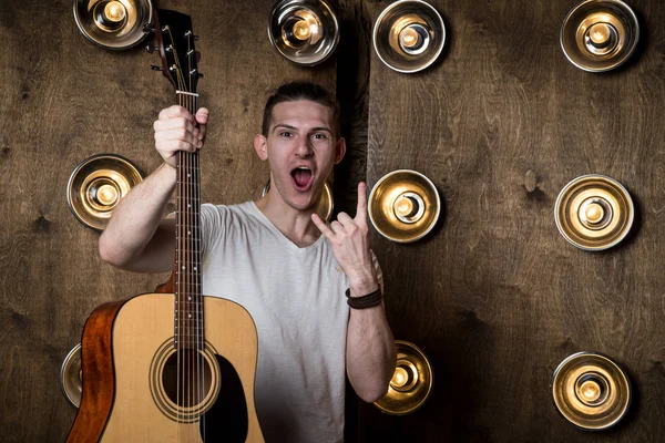 Guitarist, music. A young guy is standing with an acoustic guitar in his hand, in the background with lights behind him. Horizontal frame — Stock Photo, Image