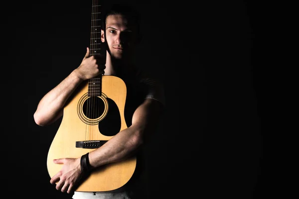 Guitariste, musique. Un jeune homme se tient debout avec une guitare acoustique sur un fond noir isolé. Cadre horizontal — Photo