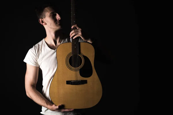 Guitarist, music. A young man stands with an acoustic guitar on a black isolated background. Horizontal frame — Stock Photo, Image