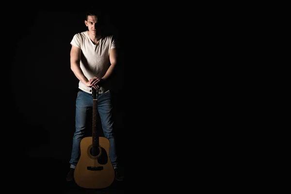 Guitarist, music. A young man stands with an acoustic guitar, on a black isolated background. Horizontal frame — Stock Photo, Image