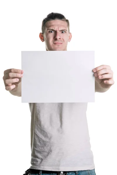 Un joven guapo con una hoja de papel en blanco mira la hoja con disgusto. Lugar para la firma, texto. Marco vertical —  Fotos de Stock