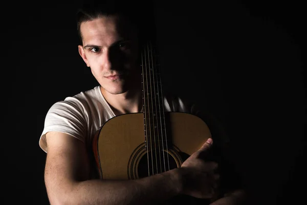 Guitarist, music. A young man stands with an acoustic guitar on a black isolated background. Horizontal frame — Stock Photo, Image