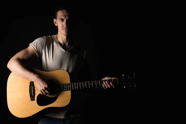 Guitarrista, música. Um jovem toca guitarra acústica num fundo preto isolado. Quadro horizontal — Fotografia de Stock