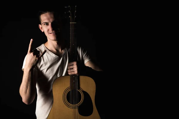 Guitarist, music. A young man stands with an acoustic guitar and shows his fingers, on a black isolated background. Horizontal frame — Stock Photo, Image