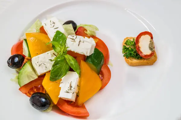 Läcker vegetarisk sallad från tomater, gurka, paprika, oliver och ost på en vit platta. Horisontell ram — Stockfoto